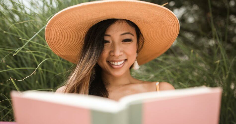 smiling woman wearing a sun hat and reading a book